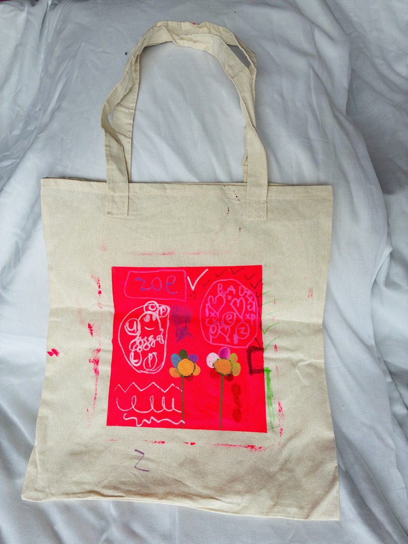 A canvas tote bag printed with a neon pink square full of drawings, flowers and the name Zoe